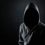 Silhouette of hooded man or hooligan over dark concrete background with copy space